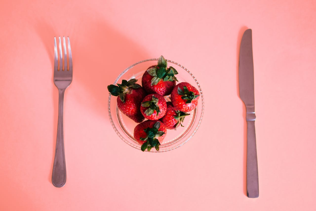 why-choose-us Bright strawberries in a bowl, laid out with silverware on a pastel pink surface. Perfect for a fresh dining concept.