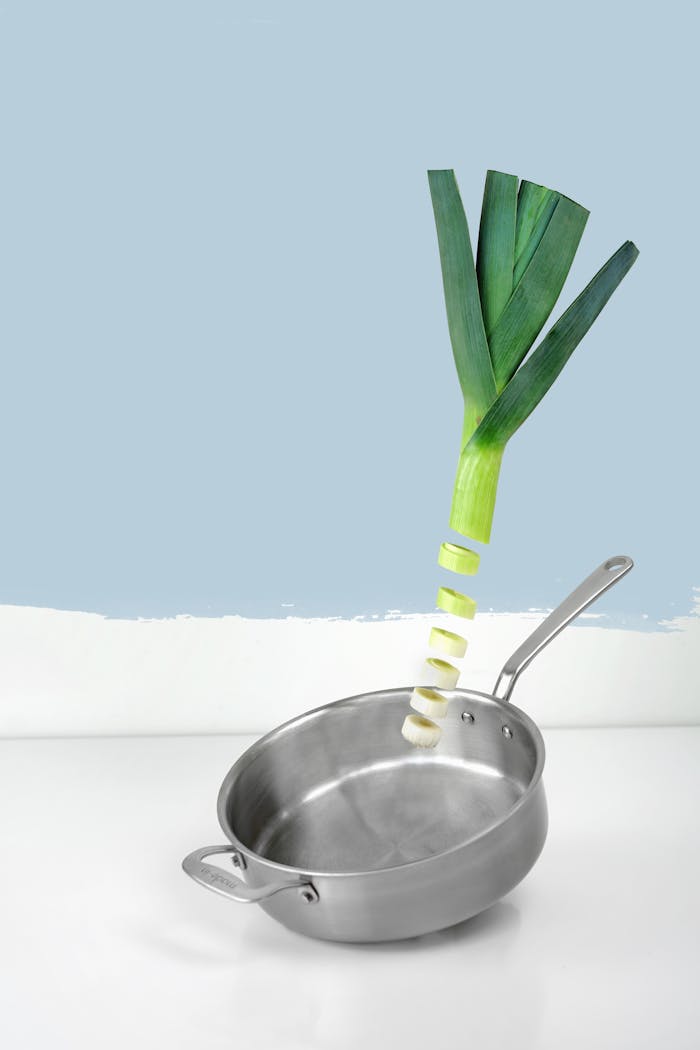 about-img Artistic presentation of a sliced leek over a stainless steel pan against a clean, blue background.