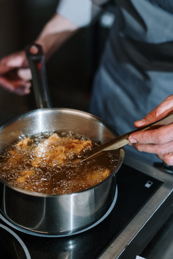 gallery-1 A close-up of a chef frying food in a saucepan on a stove, showing culinary expertise.