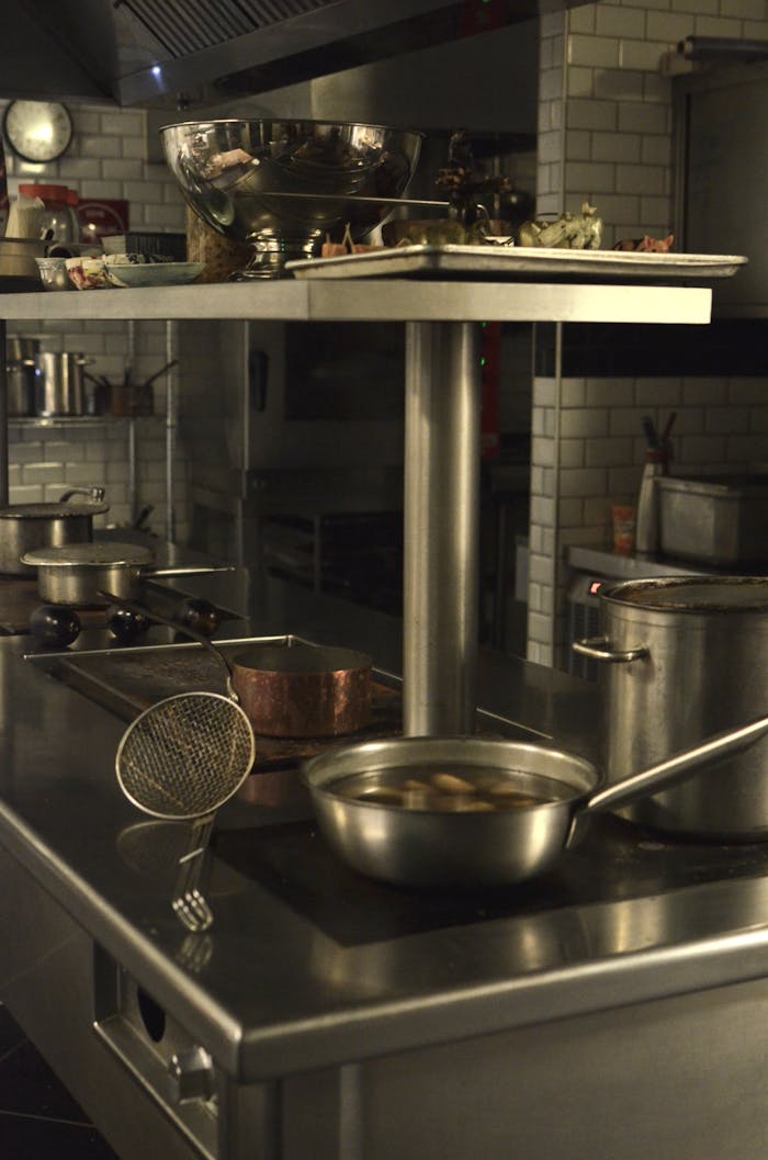 Industrial kitchen scene with pots and a fryer on a stainless steel stove.