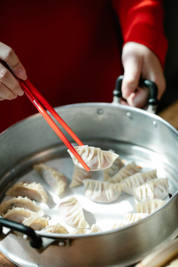 From above of crop anonymous female with chopsticks preparing Chinese dumplings in metal steamer
