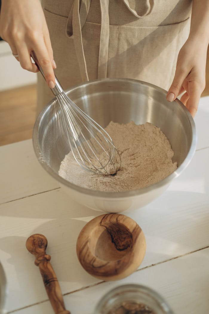 Woman preparing food with a whisk in a kitchen setting.