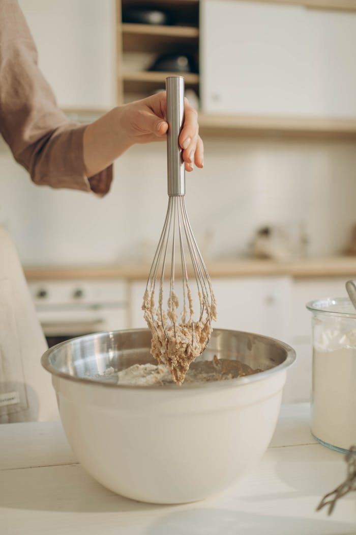 hero-img-02 A person whisking dough in a metal bowl inside a modern kitchen.